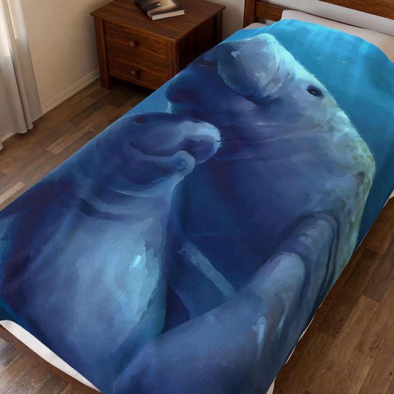 May include: A soft bed blanket featuring a large, detailed print of two manatees swimming together in deep blue water. The artwork displays the grey, rounded bodies of the marine mammals against a gradient of dark and light blue aquatic tones.