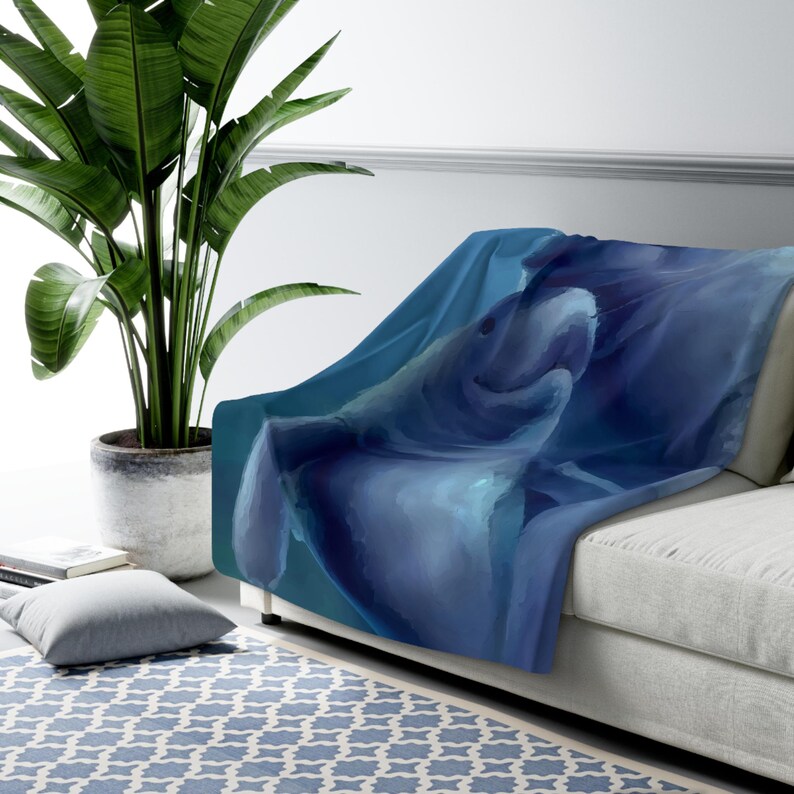 May include: A soft throw blanket featuring a detailed, painterly illustration of a manatee swimming in deep blue water. The artwork displays shades of navy, azure, and teal, capturing the gentle form of the marine mammal in a fluid, artistic style.