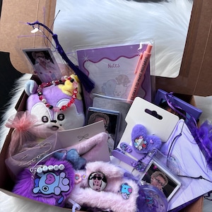 May include: A gift box filled with purple-themed stationery and accessories, including a plush character toy, a notepad labelled Notes, a pen with the text IT'S OKAY TO MAKE MISTAKES, beaded bracelets, photo cards, a fuzzy heart clip, and various character charms.