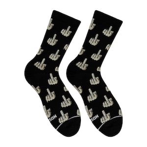 May include: A pair of black crew socks featuring a repeating pattern of white and grey middle finger hand gestures. The socks have a ribbed cuff at the top and a small white text detail near the toe area that reads SON in a bold sans-serif font.