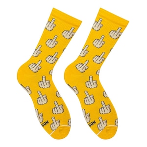 Può includere: Un paio di calzini giallo brillante con un motivo ripetuto di gesti del dito medio pixelati color beige. I calzini presentano un bordo a coste nella parte superiore e la scritta SON stampata in nero vicino alla punta di ogni calzino.