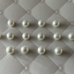 Op de afbeelding: Een verzameling van veertien individuele witte bolvormige kralen met een gladde, glanzende afwerking. De kralen zijn gerangschikt in drie horizontale rijen, met vier kralen in de bovenste rij, zes in de middelste rij en vier in de onderste rij.