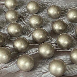 May include: A collection of numerous spherical beads with a metallic silver finish. Each bead features a smooth, reflective surface and a uniform round shape, arranged in a scattered pattern across the frame to showcase their consistent appearance.