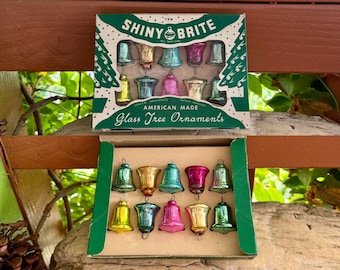 May include: Two boxes of Shiny Brite glass tree ornaments, each containing ten bell-shaped pieces in assorted metallic colors including pink, gold, blue, and green. The green cardboard packaging features white text reading Shiny Brite American Made.