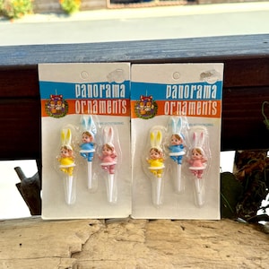 May include: A white ceramic mug with a black handle and the text "But First, Coffee" in a bold, black font. The mug is set against a blurred background, suggesting a cozy setting.