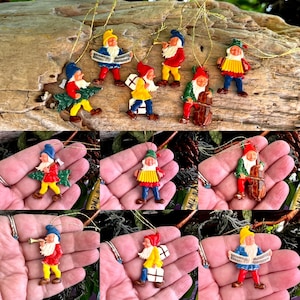 Op de afbeelding: Een set van tien vintage kerstversieringen met kleine, handgeschilderde elfjesfiguren in kleur die muziekinstrumenten bespelen. De ornamenten zijn gemaakt van metaal en hebben een glanzende afwerking.