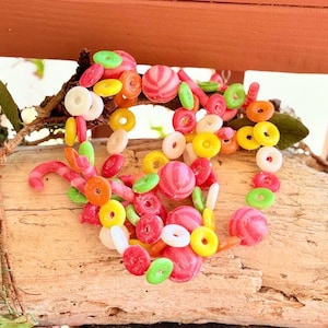 Puede incluir: Un surtido colorido de caramelos dispuestos en forma de corazón. Los caramelos incluyen bolas rosas a rayas, caramelos rojos, verdes, amarillos y blancos en forma de anillo y bastones de caramelo rosas. Los caramelos están sobre un trozo de madera.