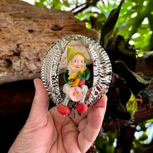 May include: A white ceramic mug with a black handle and the text "But First, Coffee" in a bold, black font. The mug is set against a blurred background, suggesting a cozy setting. The mug appears to be approximately 4 inches tall.