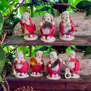 May include: A collection of seven vintage-style figurines depicting characters in red outfits with white trim, each playing a different musical instrument including a trumpet, accordion, drum, cymbals, and stringed instrument, all mounted on circular bases.