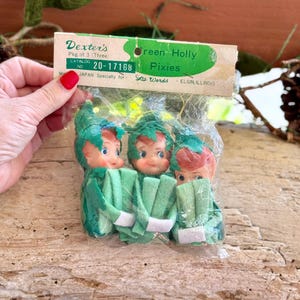 May include: A package of three Dexter's Green Holly Pixies in a clear plastic bag with a cardboard header. The header reads Dexter's Pkg. of 3 (Three) Green Holly Pixies, Catalog No. 20-17168, Made in Japan Specially for Lee Wards, Elgin, Illinois.