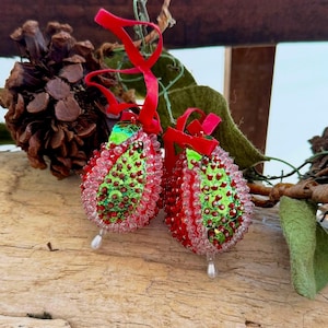 May include: Two pear-shaped ornaments featuring a green sequined center surrounded by red and clear beads. Each ornament is topped with a red ribbon loop for hanging and features a single white teardrop bead dangling from the bottom point.