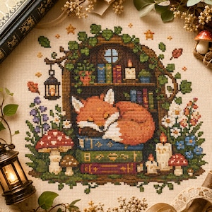 May include: A cross-stitch embroidery on cream fabric featuring a sleeping orange fox curled up on a stack of three books. The scene includes a bookshelf, a hanging lantern, various colourful wildflowers, mushrooms, and lit candles.
