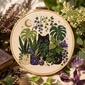 Könnte beinhalten: Ein runder Stickrahmen aus Holz mit einem Kreuzstichmotiv, das eine schwarze Katze umgeben von verschiedenen grünen Topfpflanzen, violetten Blumen, einem kleinen Zaubertrankfläschchen und einem goldenen Halbmond auf cremefarbenem Stoff zeigt.