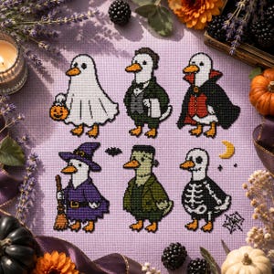 Puede incluir: Un patrón de punto de cruz sobre tela morada clara que muestra seis patos disfrazados de Halloween: un fantasma con un cubo de calabaza, un mayordomo, un vampiro, una bruja con escoba, un monstruo verde y un esqueleto, con una pequeña luna amarilla.