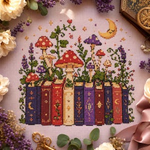 May include: A cross-stitch embroidery on light purple fabric featuring a row of colorful books with gold-colored spine details. Growing from the books are various mushrooms in red, purple, and white, green vines, and a yellow crescent moon.