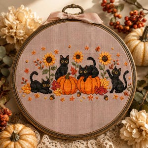 Peut inclure: Un tambour à broder circulaire contenant un motif au point de croix sur un tissu rose clair. Le dessin représente trois chats noirs, deux citrouilles orange, des tournesols jaunes et des feuilles d'automne rouges, orange et jaunes.