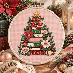 May include: A circular wooden embroidery hoop containing a cross-stitch pattern on light pink fabric. The design features a Christmas tree constructed from stacked books, decorated with a gold star, red bow, poinsettias, and ornaments.