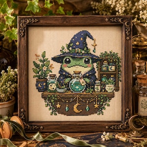 May include: A cross-stitch embroidery featuring a green frog wearing a dark blue wizard hat with gold stars, holding a glowing potion bottle. The frog sits at a wooden table with various jars, plants, and a crescent moon charm in a dark wood frame.