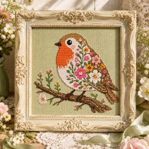 May include: A cross-stitch embroidery of a robin perched on a brown branch, set against a light green background. The bird features a bright orange chest and a body filled with colourful pink, white, and yellow floral patterns, all encased in an ornate, cream-coloured vintage-style frame.