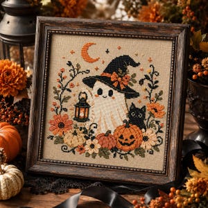 May include: A framed cross-stitch embroidery featuring a white ghost wearing a black witch hat, holding a lantern, and accompanied by a black cat and a jack-o'-lantern. The design is surrounded by orange and cream flowers, vines, and a crescent moon.