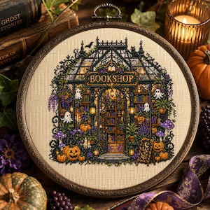 Könnte beinhalten: Ein runder Stickrahmen mit einem Kreuzstichmotiv eines Buchladens, wobei das Wort BOOKSHOP über dem Eingang steht. Das Design zeigt Bücherregale, kleine weiße Geister, orangefarbene Kürbisse, violette Pilze und grüne Ranken auf beigem Stoff.