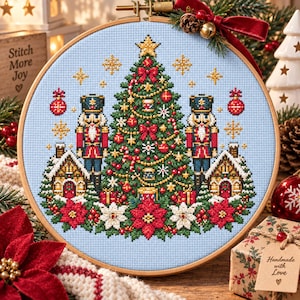 May include: A circular wooden embroidery hoop containing a cross-stitch design on light blue fabric. The pattern features a central green Christmas tree, two nutcracker figures, gingerbread houses, red poinsettias, and gold star accents.