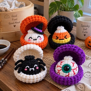 Könnte beinhalten: Vier gehäkelte Plüschtiere in Form von offenen Muschelschalen, die jeweils eine andere Halloween-Figur enthalten: ein weißes Gespenst mit Hexenhut, ein Zuckermais, eine schwarze Spinne und ein weißer Augapfel mit roten Adern, alles aus Garn.