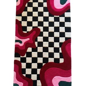 May include: A rectangular tufted rug featuring a central black and white checkered pattern flanked by organic, wavy shapes in shades of deep red, magenta, light pink, and dark forest green, creating a high-contrast, multi-colored floor covering.