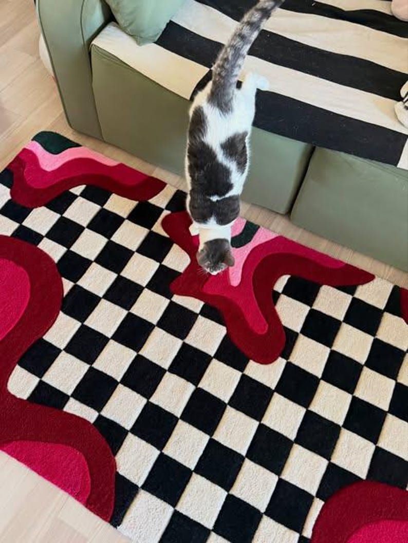 Hand tufted checkerboard rug featuring bold black and white checkered pattern with abstract pink, red, blush and burgundy wavy shapes. Modern handmade wool area rug designed for contemporary living rooms, bedrooms, apartments, dorm rooms and creative interiors. Unique dopamine decor rug with artistic retro aesthetic, colorful statement design and plush texture. Perfect for modern home decor, eclectic interiors, maximalist styling, trendy room makeover, luxury carpet styling, aesthetic room decor