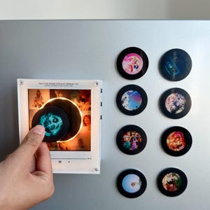 May include: A square white acrylic music player display with a glowing circular center, featuring the text "THIS IS THE SHINING STAR IN MY ORDINARY LIFE". Eight circular black magnetic discs with various colorful graphic prints are arranged nearby.