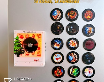 May include: A white square music player with a Christmas tree graphic and the text Merry Christmas, accompanied by 18 circular black record-style magnets featuring various holiday images. Text includes Personalized with your own photos and songs, 18 SONGS, 18 MEMORIES, 1 PLAYER + 18 CUSTOM RECORDS, and 18 Photos • 18 Songs.