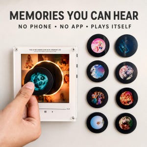 May include: A white square music player frame with a central circular slot, displaying the text "MEMORIES YOU CAN HEAR" and "NO PHONE • NO APP • PLAYS ITSELF". Eight circular black discs with various colorful graphic prints are arranged to the right.
