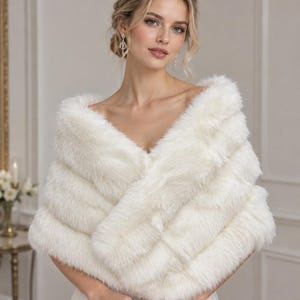 May include: A white faux fur stole featuring a thick, plush texture that wraps around the shoulders. The garment has a soft, voluminous appearance with long, dense fibers and a V-neckline drape. The text CultivateRomania is visible in the corner.