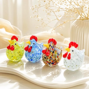 Puede incluir: Cuatro pequeñas figuras de pollo de cristal dispuestas en fila. Cada pollo presenta una cresta y barbillas de color rojo brillante, un pico amarillo y ojos negros. Los cuerpos están hechos de vidrio moteado con patrones en verde lima, azul claro, multicolor y blanco.