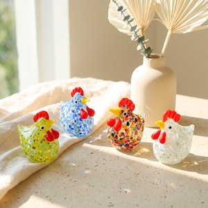 May include: Four small glass chicken figurines featuring speckled patterns in yellow, blue, multicolored, and white. Each bird has a bright red comb and wattle with a yellow beak. The glass bodies are translucent with colorful flecks throughout.