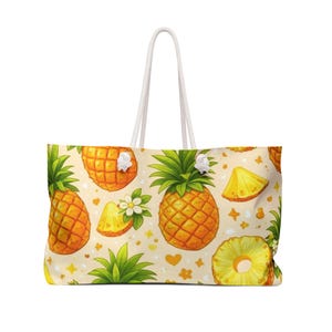 Può includere: Una borsa tote con un motivo ripetuto di ananas gialli, ciuffi verdi, fette di ananas e piccoli fiori bianchi su sfondo color crema chiaro. La borsa presenta due manici in corda bianca fissati nella parte superiore con nodi bianchi.
