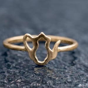 Könnte beinhalten: Ein goldfarbener Ring mit einem ausgeschnittenen Design in Form einer Teekanne. Das Band hat eine glatte, matte Oberfläche und auf der Innenseite des Rings ist deutlich der Text 14KGP eingeprägt, der die Metallzusammensetzung des Schmuckstücks angibt.