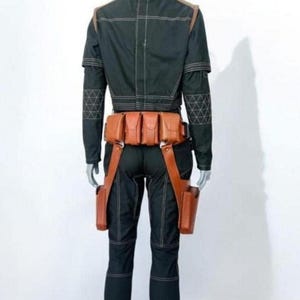Pu&ograve; includere: Una giacca nera a maniche lunghe e pantaloni abbinati con cuciture bianche a contrasto e motivi geometrici sulle maniche. Una cintura multiuso in pelle color cuoio con diverse tasche e due fondine da coscia &egrave; indossata in vita.