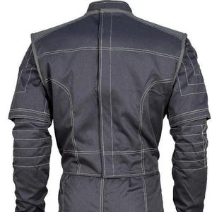 May include: A dark charcoal gray jacket featuring a high collar and a vertical center back closure. The garment is detailed with prominent white contrast stitching that outlines the shoulders, sleeves, and back panels, creating a structured look.