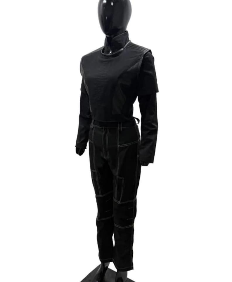 May include: A black long-sleeved top with a high collar and a front zipper, paired with matching black trousers featuring prominent white contrast stitching. The trousers have a multi-panel construction with visible seams along the legs and waist.