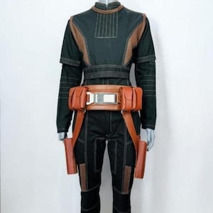 Pu&ograve; includere: Una maglia nera a maniche lunghe e pantaloni abbinati con inserti in similpelle color cuoio e cuciture bianche. Una cintura multiuso color cuoio con due tasche laterali e due attacchi verticali a fondina &egrave; indossata in vita sopra l'indumento.