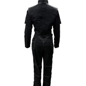 May include: A black jumpsuit featuring a high collar, long sleeves, and a structured bodice. The pants portion includes prominent white contrast stitching along the seams, a V-shaped waist detail, and horizontal stitching lines across the legs.