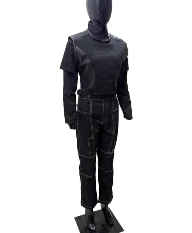 May include: A black long-sleeved top with a high collar and matching black trousers featuring prominent white contrast stitching. The trousers have a structured design with reinforced knee panels and a belt loop waistband, displayed on a mannequin.