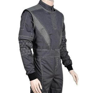 May include: A dark gray racing suit featuring a high collar, long sleeves with black ribbed cuffs, and white contrast stitching. The torso includes diagonal panels and a wide waistband, while the sleeves display a geometric triangular pattern.