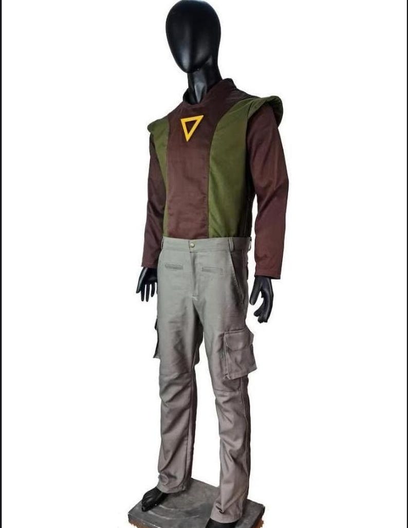 May include: A long-sleeved shirt featuring a brown and olive green color-blocked design with a yellow triangle emblem on the chest, paired with light gray cargo pants that include side pockets, displayed on a black mannequin against a white background.