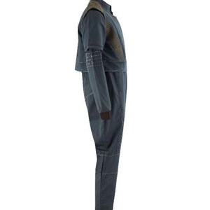 Puede incluir: Un mono de color gris oscuro con cuello alto, mangas largas con pu&ntilde;os marrones y un panel texturizado marr&oacute;n en la parte superior del pecho. La prenda presenta detalles de costuras blancas visibles a lo largo de las costuras, los hombros y las piernas.