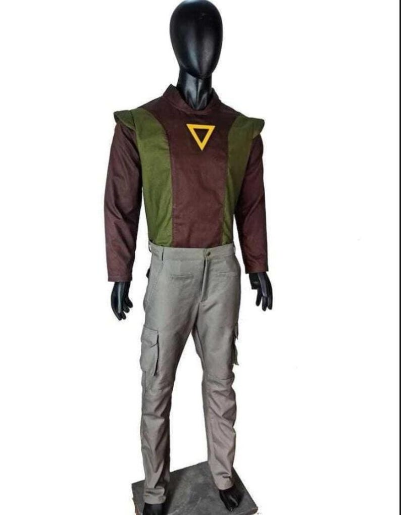 May include: A long-sleeved shirt featuring a brown center panel and olive green side panels with a yellow triangle emblem on the chest, paired with light gray cargo pants. The outfit is displayed on a black mannequin against a white background.