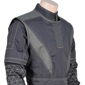 May include: A dark gray tactical-style shirt featuring a high collar, vertical stitched panels on the chest, and reinforced shoulder sections. The sleeves display a white geometric grid pattern, while the torso includes light gray contrast stitching.