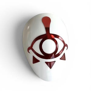 May include: A smooth, white, oval-shaped mask featuring a prominent, glossy, metallic red graphic design. The design consists of a stylised eye symbol centred on the forehead area, with three small red triangles pointing downward below the eye.