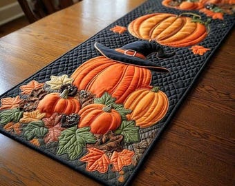 May include: A quilted table runner featuring a black background with an orange pumpkin pattern. The design includes pumpkins in various sizes, some wearing black witch hats, surrounded by appliqued fabric leaves in shades of green and orange.